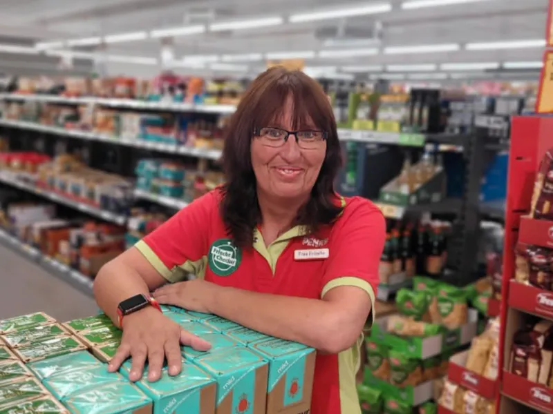 Claudia Fritsche steht lächelnd im PENNY Markt auf der Verkaufsfläche und blickt in die Kamera