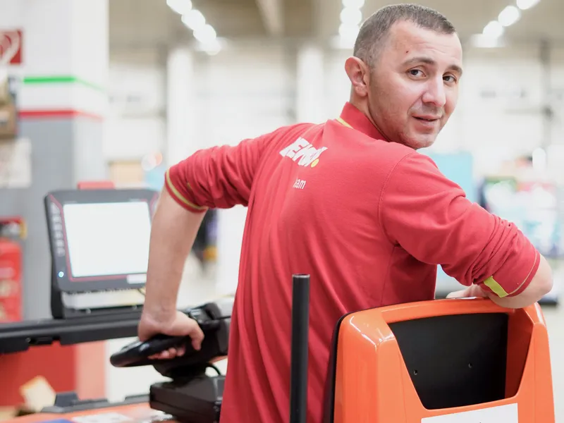 Mehmet Caliskan sitzt in Arbeitskleidung auf einem Schlepper im Lager und dreht sich zur Kamera