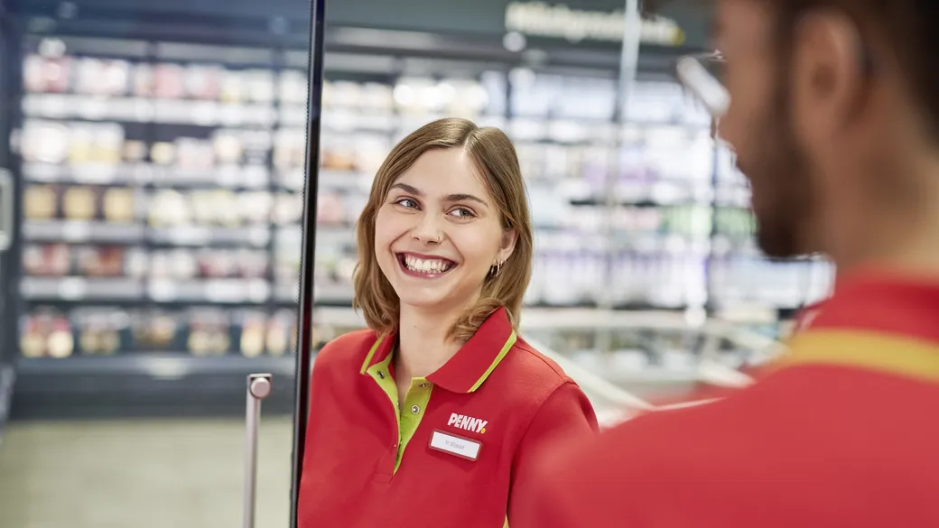 Eine lächelnde PENNY Mitarbeiterin steht am Kühlregal im Markt